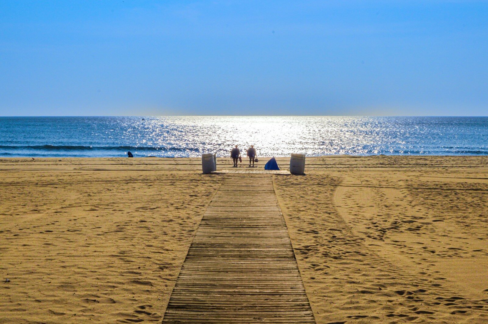 Wooden path leads to people on a sunny beach.